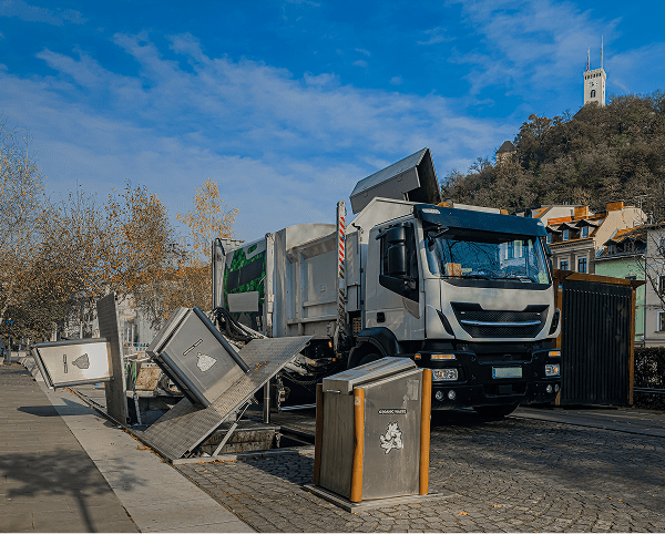 Garbage truck unloading waste into a dumpster on the street.