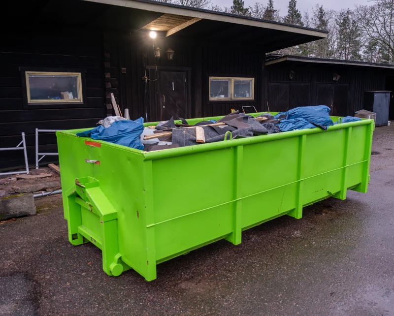 A large green dumpster filled with various waste outdoors.