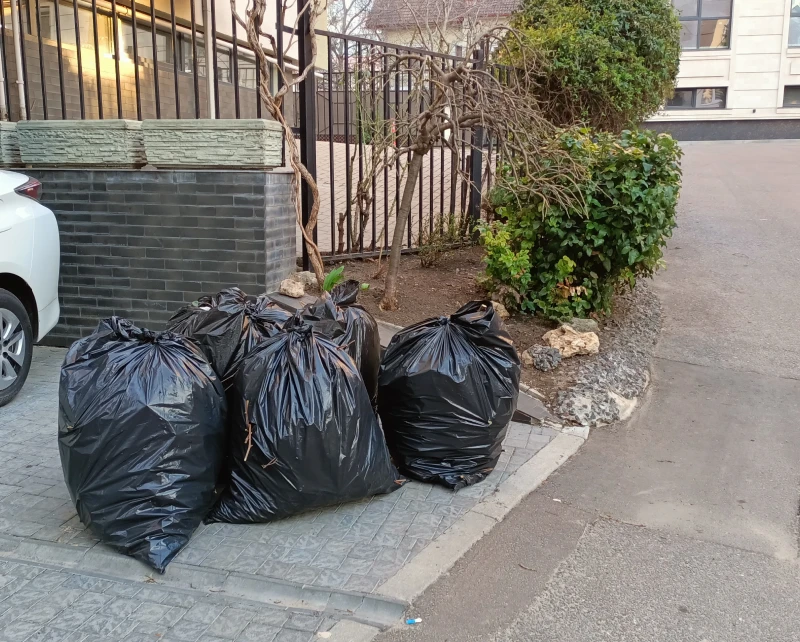 Three black garbage bags placed on a sidewalk beside a building.