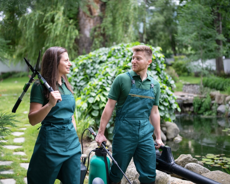 Two gardeners in green uniforms are having a conversation outdoors.
